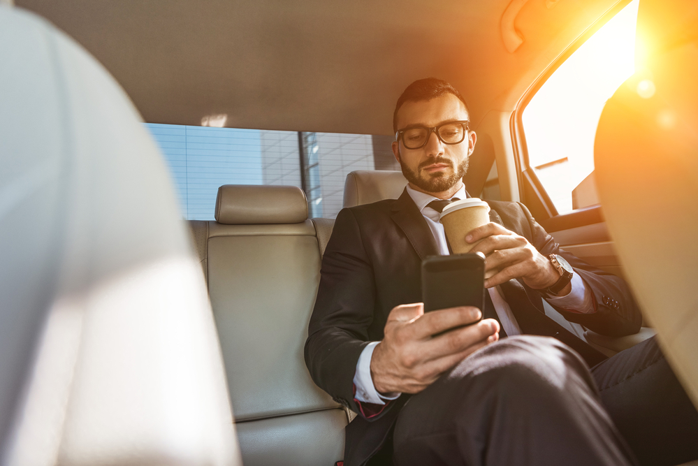 朝日が差し込む車の後部座席でコーヒーを飲むビジネスマン