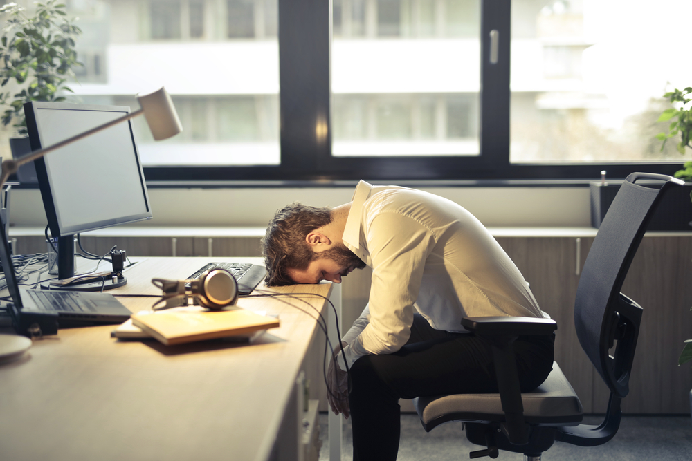 睡眠不足で体調が悪く机に突っ伏すビジネスマン