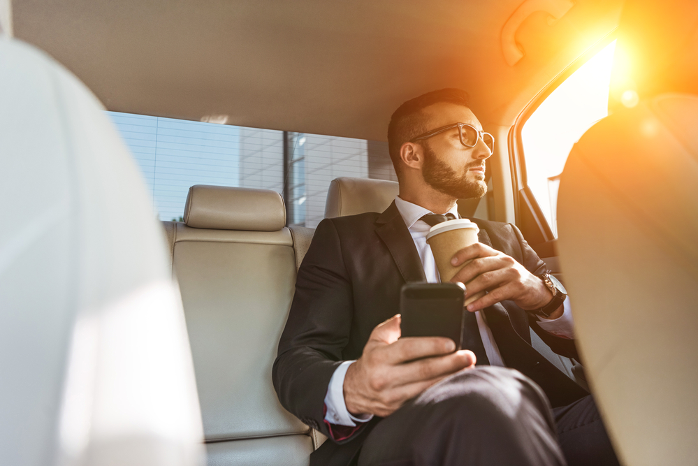 車の中で朝日を浴びながらコーヒーを飲むビジネスマン